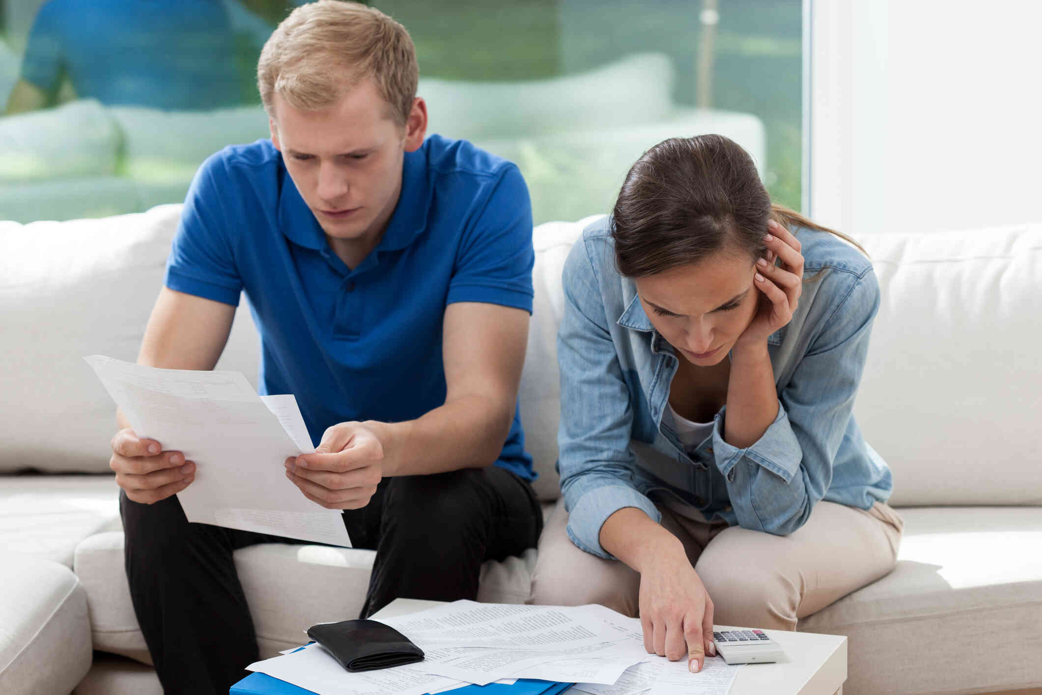 A couple sits together, focused on the documents, appearing stressed.